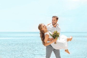 Wall Mural - Happy groom holding bride in his arms on seashore