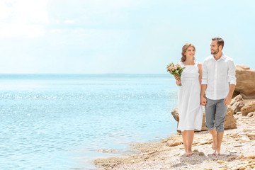 Wall Mural - Happy newlywed couple walking on rocky beach