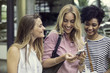 © PhotoAlto - Young woman looking at smartphone and chatting with friends outdoors