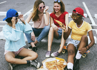 A diverse group of women sitting on the floor and eating pizza together