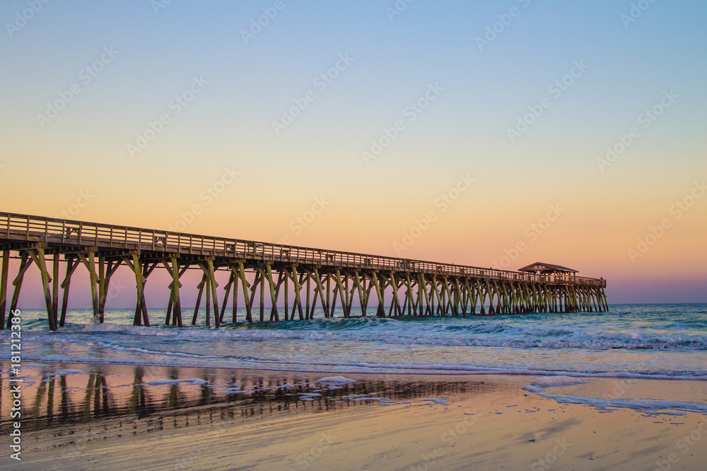 Myrtle Beach Ocean Pier Background. Sunset colors on the coast of Myrtle Beach, South Carolina with as waves crash on the Atlantic coast beach. - obrazy, fototapety, plakaty 