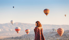 A Tourist Girl On A Mountain Top Enjoying Wonderful View Of The Sunrise And Balloons In Cappadocia. Happy Travel In Turkey Concept