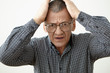 Portrait of stressed desperate senior male in checkered shirt and eyeglasses holding hands on his head, feeling nervous because of problem. Elderly people, stress, negative emotions and reaction