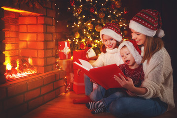 Wall Mural - family mother and children read a book at christmas near fireplace at home