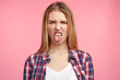 Dissatisfied female model frowns face, has disgusting expression, shows tongue, expresses non compliance, irritated with somebody, rejects do something. People and negative facial expressions