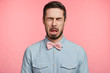 © wayhome.studio  - Bearded brunet attractive man closes eyes and opens mouth sees something sour, isolated over pink background. Unhappy handsome young male wears pink bow tie and shirt, makes grimace or pulls face