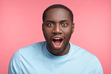 Wall Mural - Emotional attractive Afro American male stares at presentation of new racing car, wants buy or try it, keeps jaw dropped and eyes widely opened, admires speed and comfort, has rapt attention