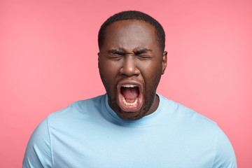 Wall Mural - Dark skinned emotional male screams or yells, opens mouth widely, closes eyes, being in panic or stressful situation, horrified to see, hear something. Negative emotions and expressions concept