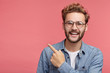 © wayhome.studio  - Stylish unshaven man in denim shirt points at copy space on pink wall as shows something pleasant, has smiling look, advertises product. Look over here! People, advertising, emotions concept