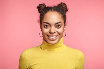 Horizontal portrait of good looking African female with appealing appearance smiles happily, has good mood after spending weekends in restaurant with friends, glad and pleased to pose at camera