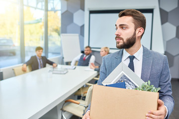 Wall Mural - Portrait of sad bearded businessman holding box of personal belongings being fired from work, copy space