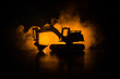 © zef art - silhouette tracked excavator on dark foggy red orange sky background with toy car. Empty space