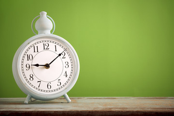 Retro alarm clock on wooden board with green background