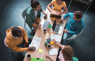 Aufkleber - Top view outgoing young startup team working together while sitting at table. Different digital devices and copybooks are on it. Occupation concept