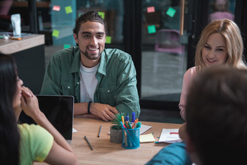 Aufkleber - Portrait of cheerful unshaven man telling with beaming female comrades while situating at desk in office. Work concept