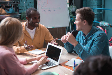Poster - Portrait of cheerful man talking with side view comrade while locating at table in room. Job concept