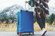 © Alex from the Rock - Traveling woman wearing poncho with bright blue suitcase standing next to stunning mountain wild. Wanderlust and boho style
