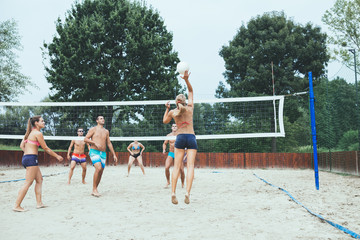 Group of young people playing beach volleyball on beautiful sunny day.