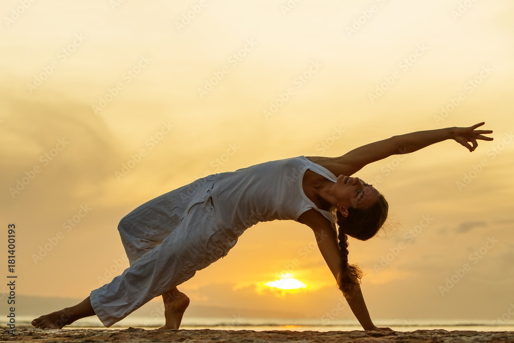 Woman practices yoga at the seashore at sunset on Bali in indonesia - obrazy, fototapety, plakaty 