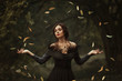 Incredible, amazing, seductive girl, in a black dress , magic rotates the leaves. background is fantastic autumn. Artistic photography. Fantasy gothic woman dark queen. Lady medieval witch