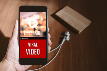 Aufkleber - Hand holding mobile watching viral video advertising on phone screen at blur wood table,share video on social media concept,Digital marketing strategy.