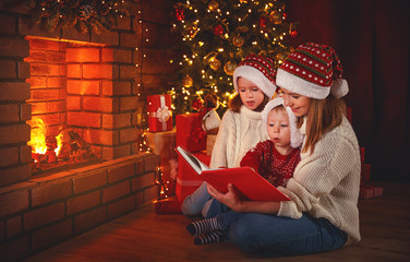 Wall Mural - family mother and children read a book at christmas near fireplace at home.