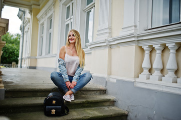 Blonde girl wear on jeans with backpack posed against vintage house.