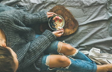 Healthy winter breakfast in bed. Woman in grey sweater and jeans eating rice coconut porridge with figs, berries, hazelnuts, top view, copy space. Clean eating, alkaline diet, comfort food concept