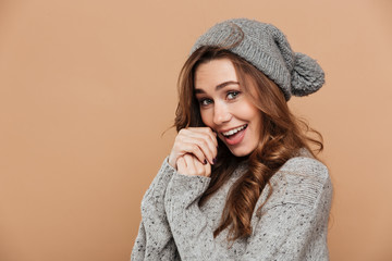 Wall Mural - Close-up photo of cute brunette woman in gray sweater and hat warming hands and looking at camera