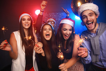 Celebrating New Year together. Group of beautiful young people in Santa hats throwing colorful confetti, looking happy