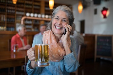 Wall Mural - Smiling senior woman talking on mobile phone while having glass