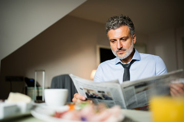 Wall Mural - Mature businessman having breakfast in a hotel room.