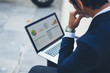 © SFIO CRACHO - Attractive elegant businessman using contemporary notebook sitting outside the office.Graphs and diagramm on laptop screen.Blurred background. Horizontal.