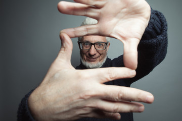 Fabulous at any age. Eyewear concept. Portrait of a handsome mature man looking at camera through frame made of his hands. Close up. Studio shot