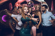 © VadimGuzhva - A woman in a green dress is singing songs with her friends at a karaoke club. Her friends have fun on the background.