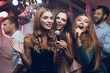 © VadimGuzhva - Three beautiful girls sing in a karaoke club. Behind them are men waiting for their turn.