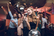 Young people have fun in a nightclub and sing in karaoke. In the foreground there is a woman in a black dress.