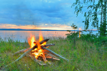 Wall Mural - Big night bonfire on the riverbank at sunset, dawn.