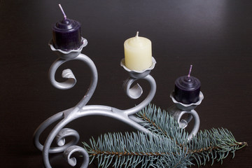 The branches of the blue spruce lie on the plane. Among them, candles are white and black on a forged candlestick.