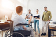 © VadimGuzhva - A man in a wheelchair is showing documents to his team in office. The are working in a bright modern office.