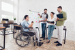 © VadimGuzhva - Office workers and man in a wheelchair discussing business moments while working in a modern office.