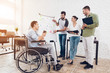 © VadimGuzhva - Office workers and man in a wheelchair discussing business moments while working in a modern office.