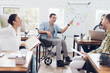 © VadimGuzhva - Office workers and man in a wheelchair discussing business moments in a modern office.