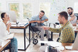 © VadimGuzhva - Office workers and man in a wheelchair discussing business moments in a modern office.