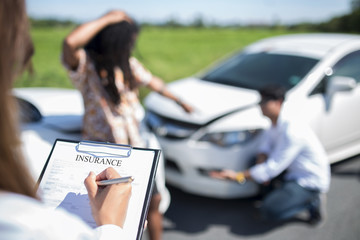 Side view of writing on clipboard while insurance agent examining car after accident