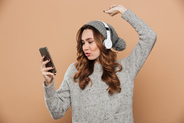 Canvas Print - Cute young woman with curly hairstyle holding smartphone while listening to music