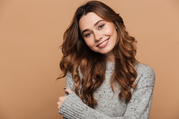 Wall Mural - Close-up portrait of cheerful brunette woman in gray knitted sweater looking at camera, isolated on beige background