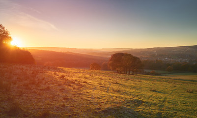 Wall Mural - red, orange and yellow glow of a sunset over green pastures and trees in the english countryside. gi