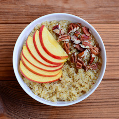 Wall Mural - Fruit and nut Breakfast quinoa porridge. Quinoa porridge with fresh apples and pecans in a white bowl isolated on wooden background. Closeup. Top view