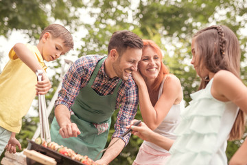 Father teaching son cooking on barbecue with family in background